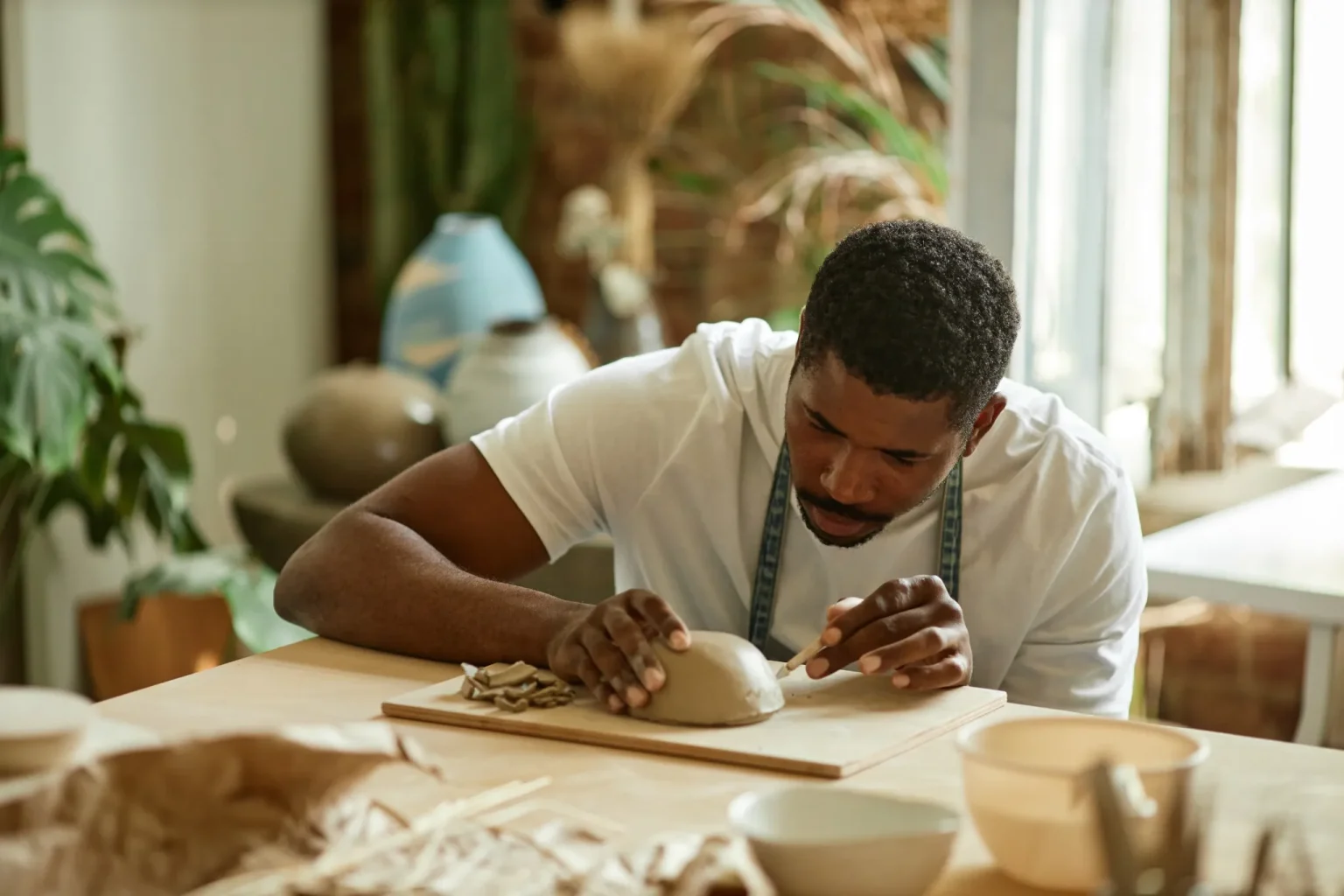 Un homme est concentré sur la création d'une pièce en céramique ou en poterie. Il porte un tablier.