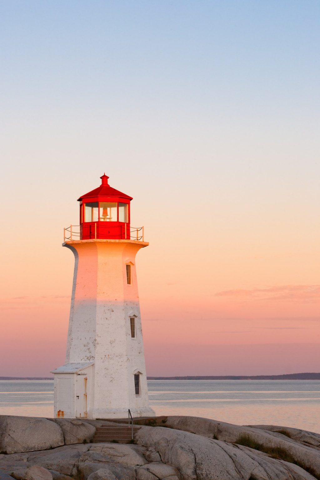 photo d'un phare enraciné sur des rochers avec le coucher du soleil en arrière plan. Les couleurs sont douces et la mer calme. Cette photo symbolise la définition d'un objectif professionnel qui donne une direction à notre carrière