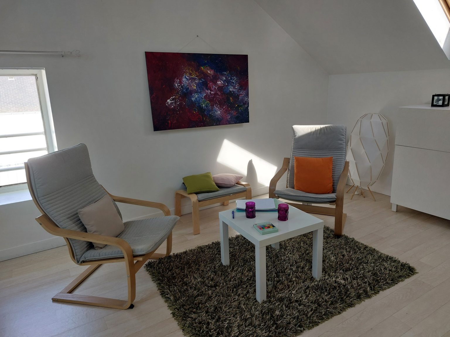 bureau cocooning avec deux grands fauteuils, des coussins colorés un tapis douillet et un cadre au mur, il y a un raon de lumière qui traverse la pièce.